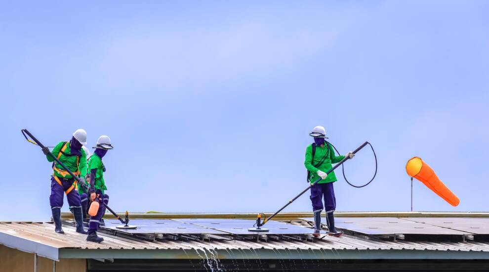 Group of professional cleaning service workers clean the solar panels on industrial building roof
